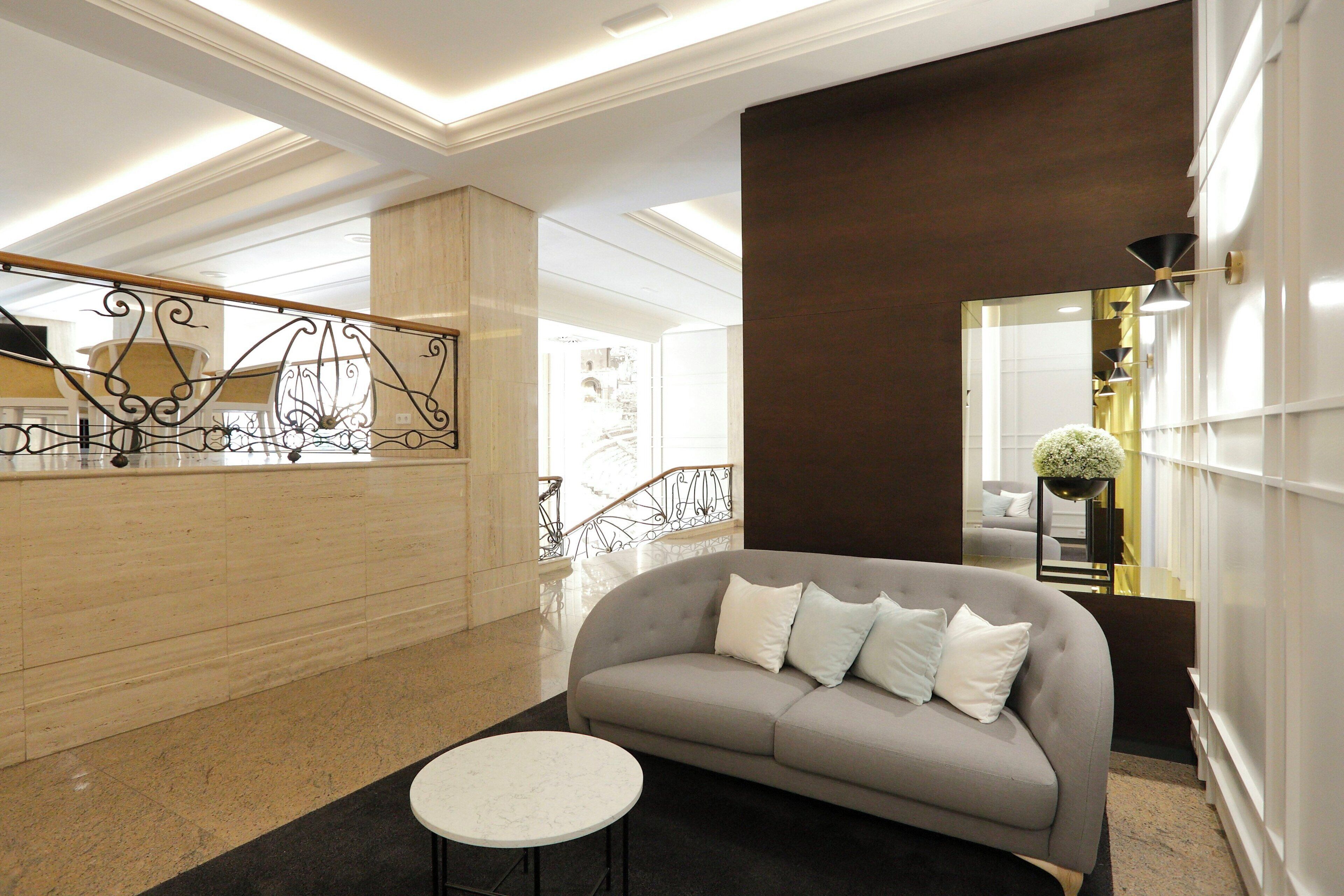 A modern lobby with a grey sofa, a round white table, and a decorative metal railing.