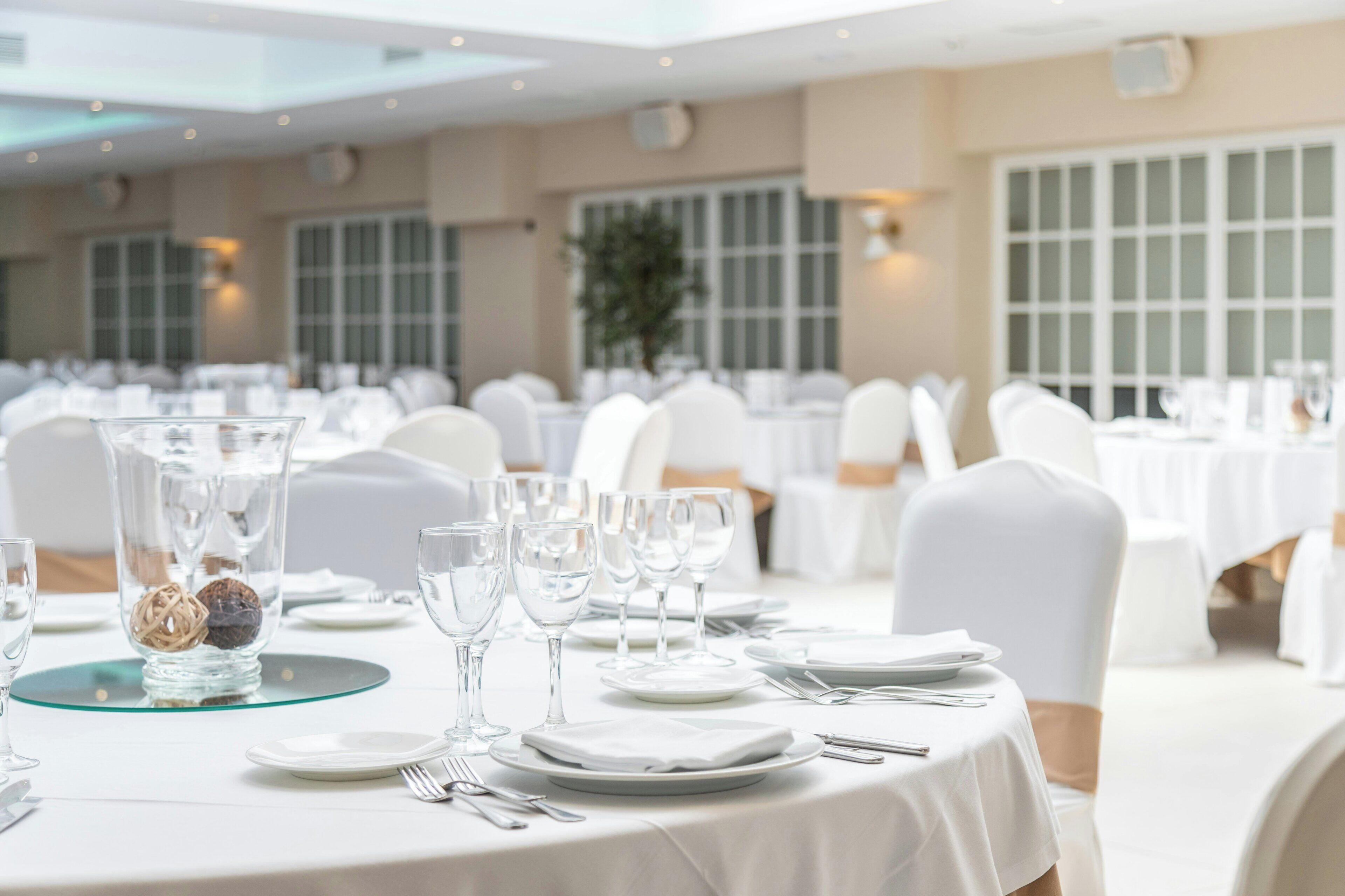 A banquet hall with round tables set for dining, white tablecloths, and chairs with white covers.