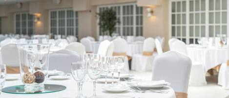 A banquet hall with round tables set for dining, white tablecloths, and chairs with white covers.