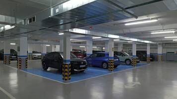 Un estacionamiento de varios niveles con coches estacionados en espacios designados, columnas estructurales visibles e iluminación elevada.