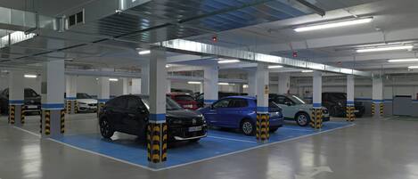 A multi-level parking garage with cars parked in designated bays, visible structural columns, and overhead lighting.