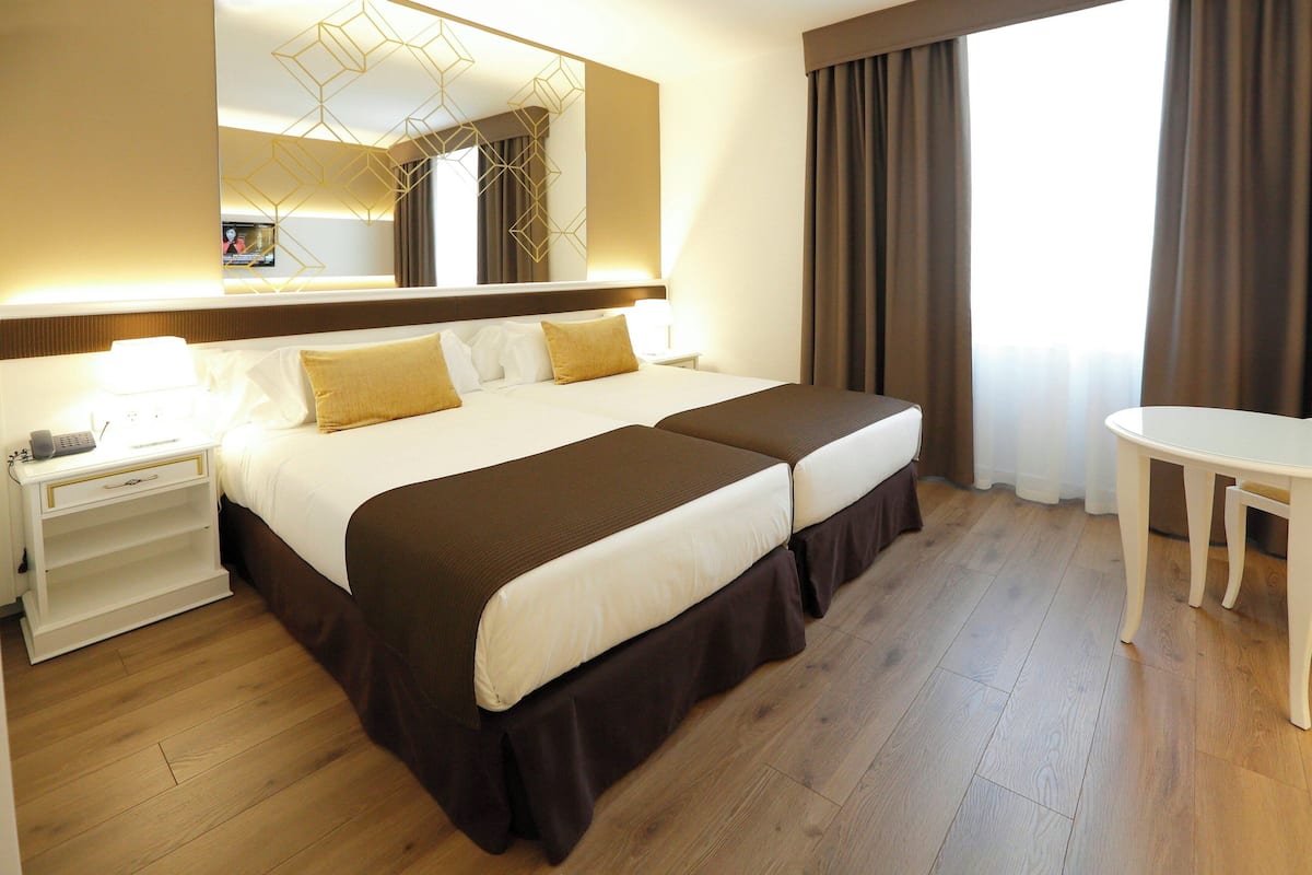 A hotel room with a large bed, bedside tables, a desk, a mirror, and a view of the outdoors.