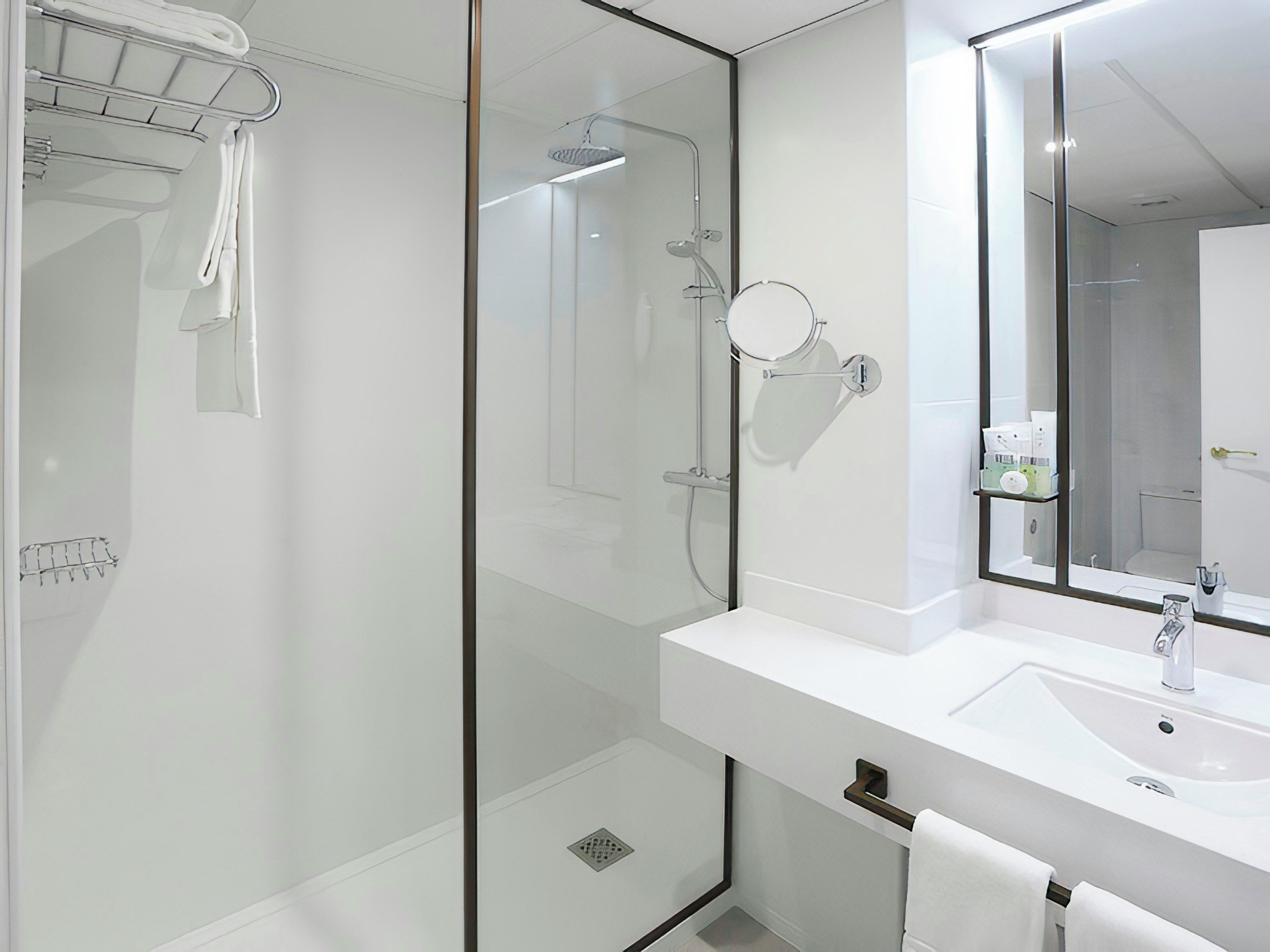 Un baño moderno con ducha envuelta en vidrio, un lavamanos blanco y un espejo grande.