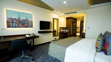 A hotel room with a bed, a desk, a chair, a TV, a mirror, and a painting on the wall.