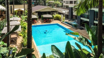 A rectangular swimming pool with a person swimming, surrounded by palm trees and outdoor furniture.