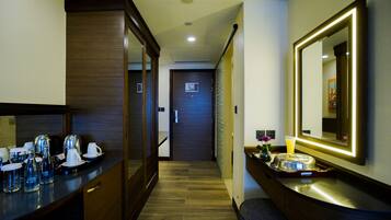Un pasillo de hotel con suelo de madera, una recepción con máquinas de café, un espejo y una puerta con un letrero.