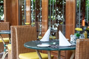 A dining area with wicker chairs and a round table set with a plate, cutlery, and napkins.
