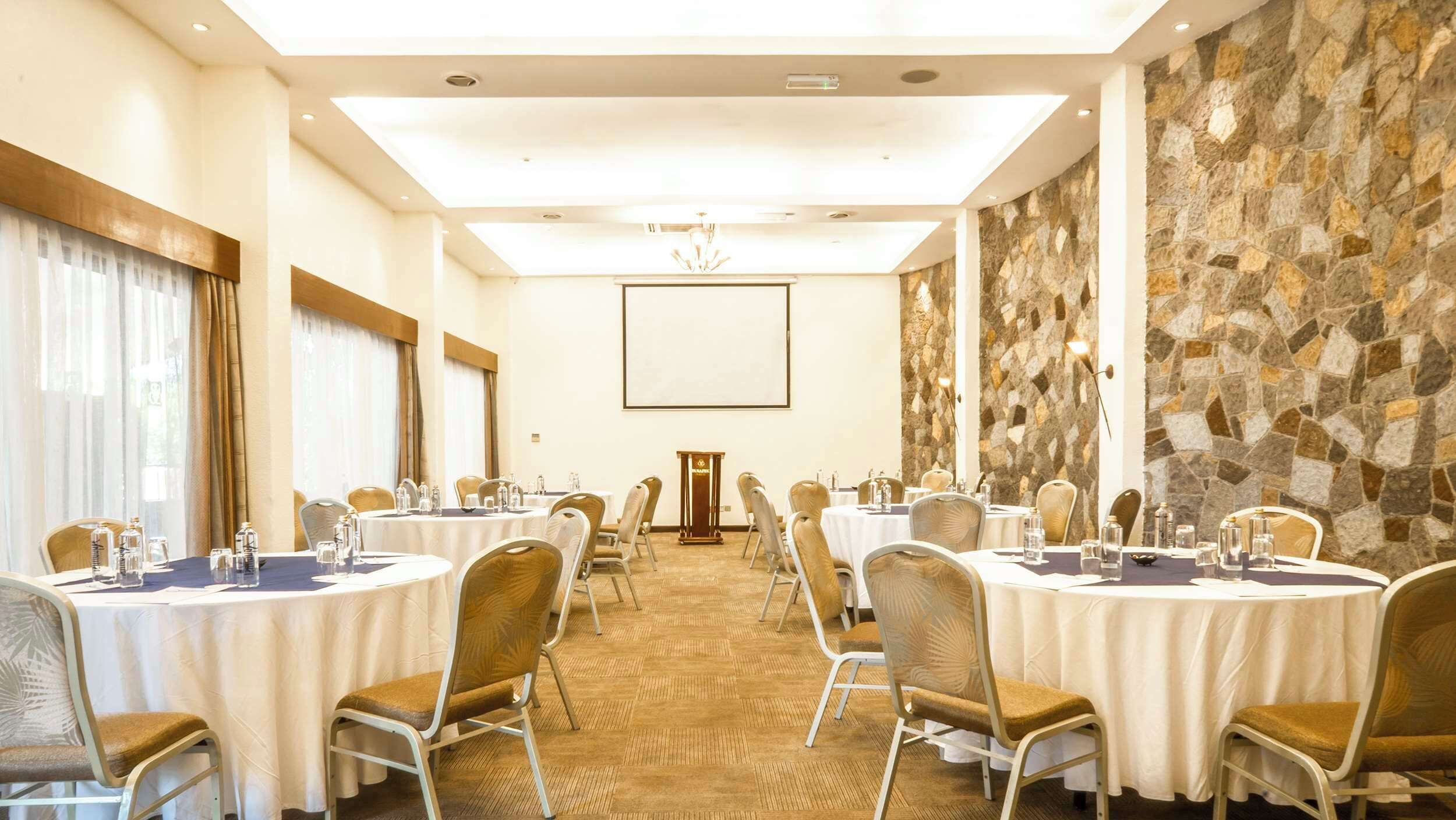 A conference room with round tables, chairs, and a stone wall.