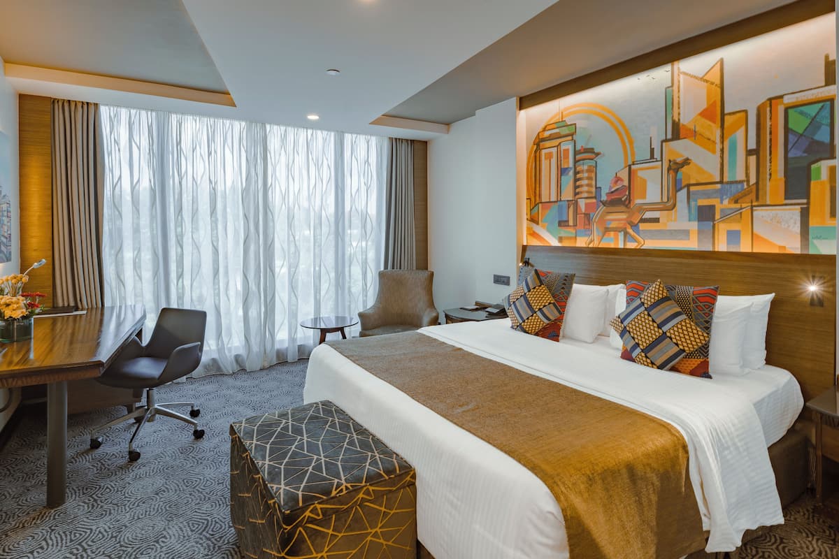 Ein Hotelzimmer mit einem großen Bett, einem Schreibtisch, einem Sessel und einem Gemälde an der Wand.