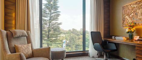 A modern hotel room with a large window, a comfortable sofa, a desk with a chair, and a decorative wall piece.