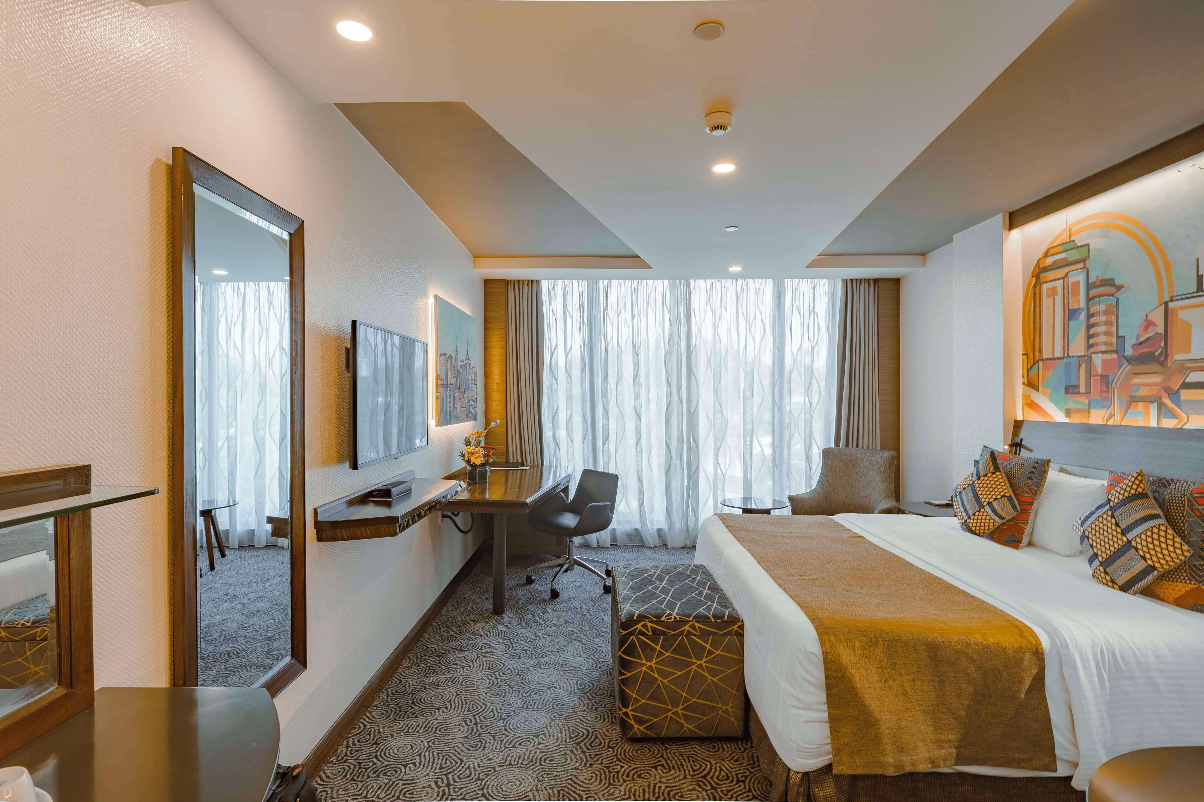 A hotel room with a large bed, a desk, a chair, a mirror, and a window with curtains.
