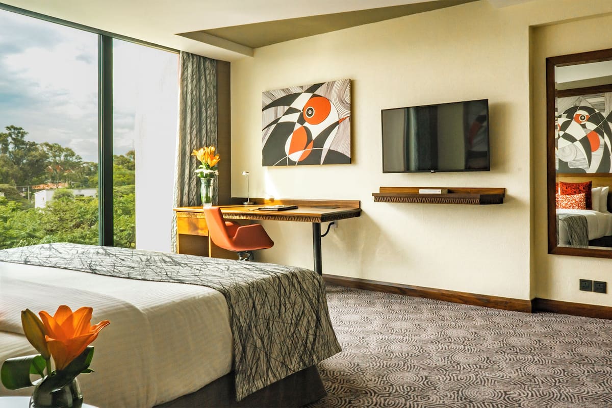 Ein Hotelzimmer mit Bett, Schreibtisch, Stuhl, Fernseher und großen Fenstern mit Blick ins Freie.