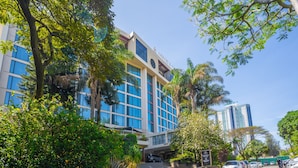 A modern hotel with a large glass facade, surrounded by lush greenery and palm trees. - Sarova Panafric Hotel, Nairobi Upper Hill (Nairobi)