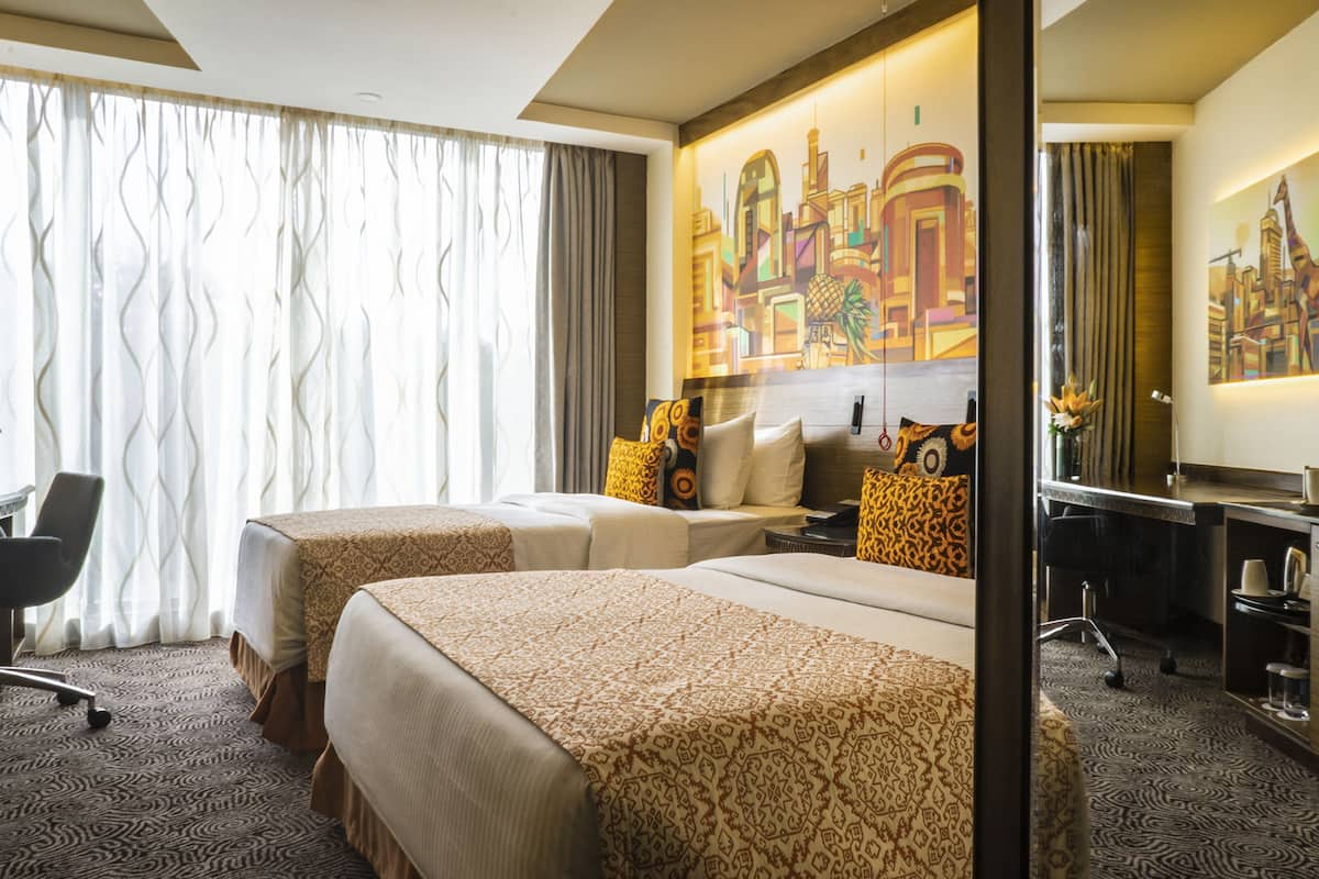Ein Hotelzimmer mit zwei Betten, einem Schreibtisch, einem Stuhl, einem Spiegel und einem großen Gemälde an der Wand.