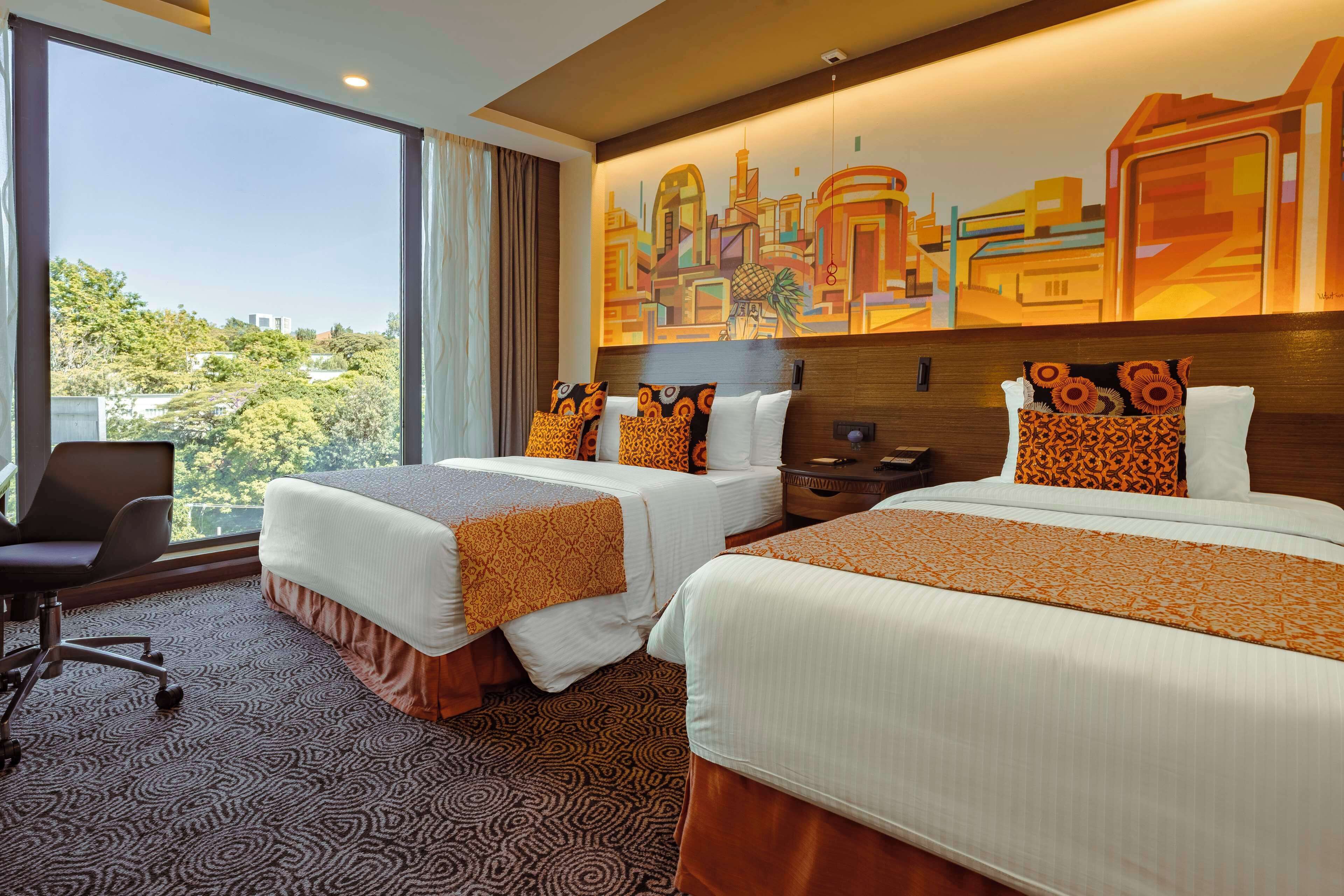 Habitación de hotel con dos camas, un escritorio y una silla. Amplia ventana con vista a la ciudad.