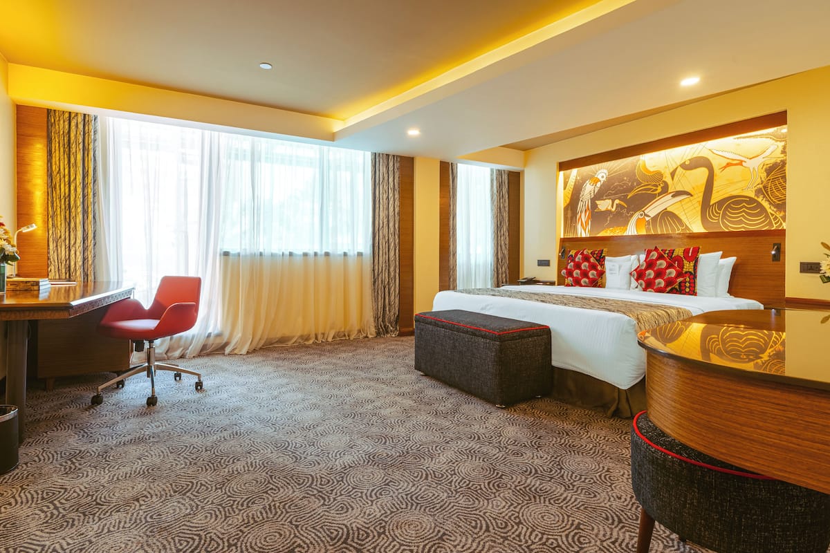 Ein Hotelzimmer mit einem großen Bett, einem Schreibtisch, einem roten Sessel und Teppichboden.