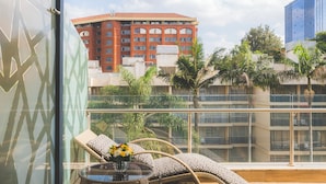 A balcony with wicker furniture, a glass table with a vase of flowers, and a view of buildings in the background. - Sarova Panafric Hotel, Nairobi Upper Hill (Nairobi)