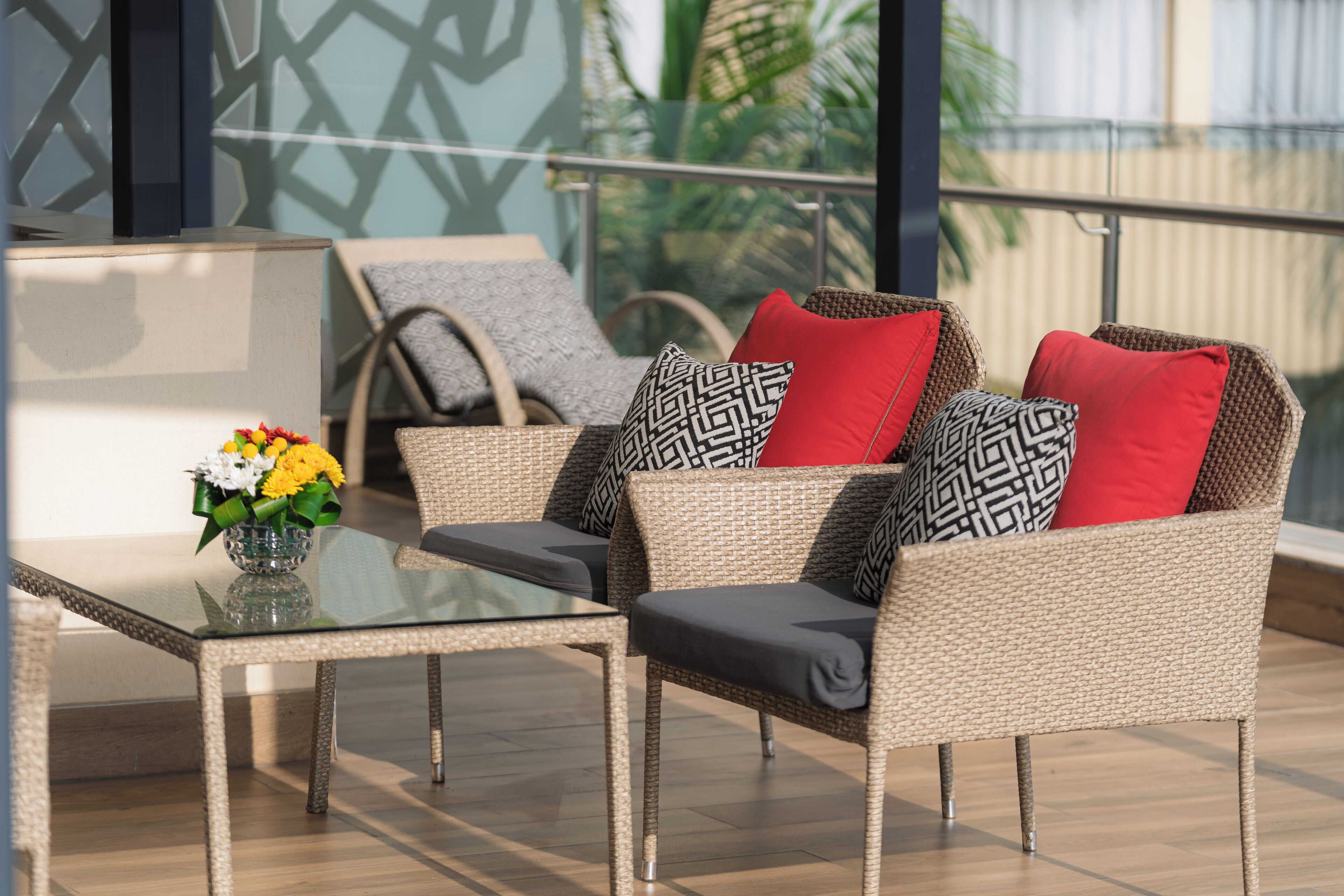 A balcony with wicker furniture, a glass table, and a vase of flowers.