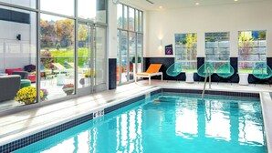An indoor swimming pool with clear glass walls, a tiled edge, and a view of the outdoors. - Aloft by Marriott Framingham (Framingham)