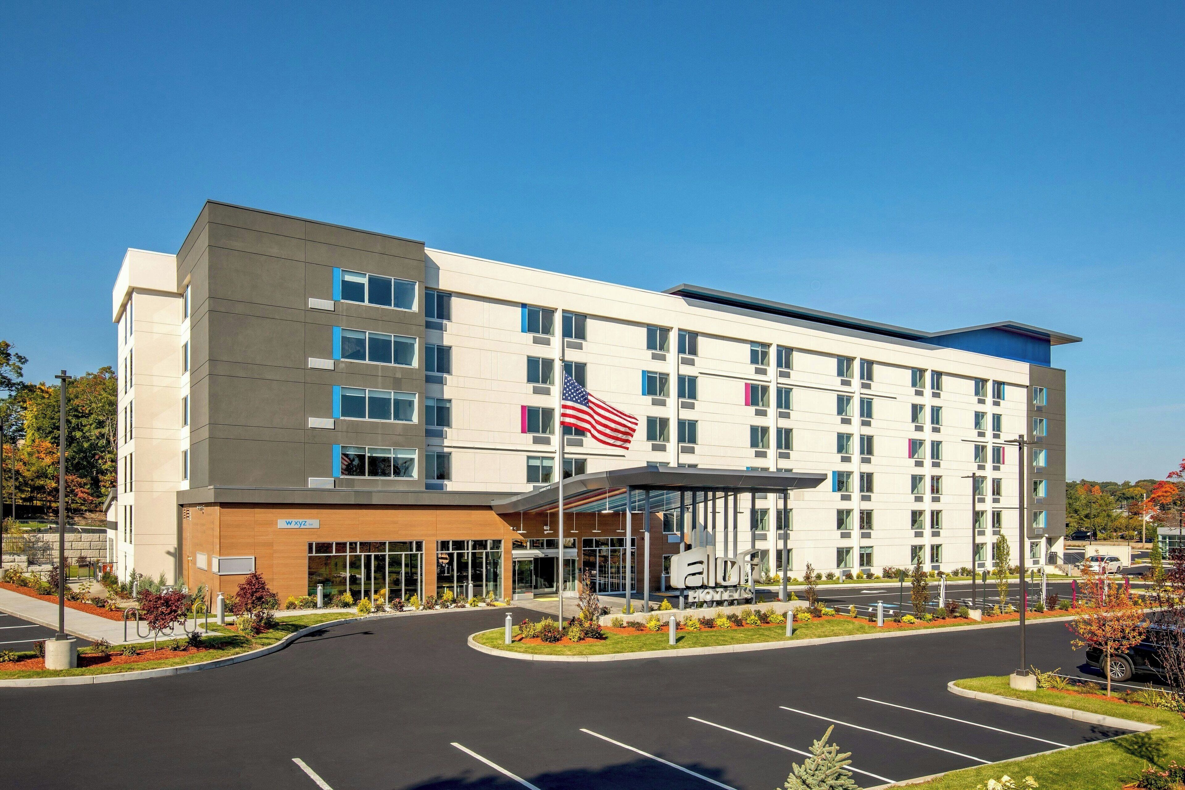 A modern hotel with a flat roof, multiple floors, and a covered entrance.