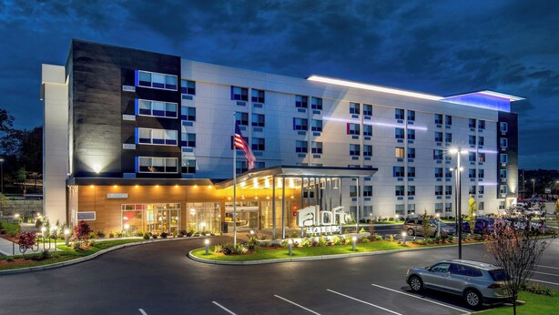 A modern hotel with a prominent entrance, multiple floors, and a well-lit facade. - Aloft by Marriott Framingham (Framingham)