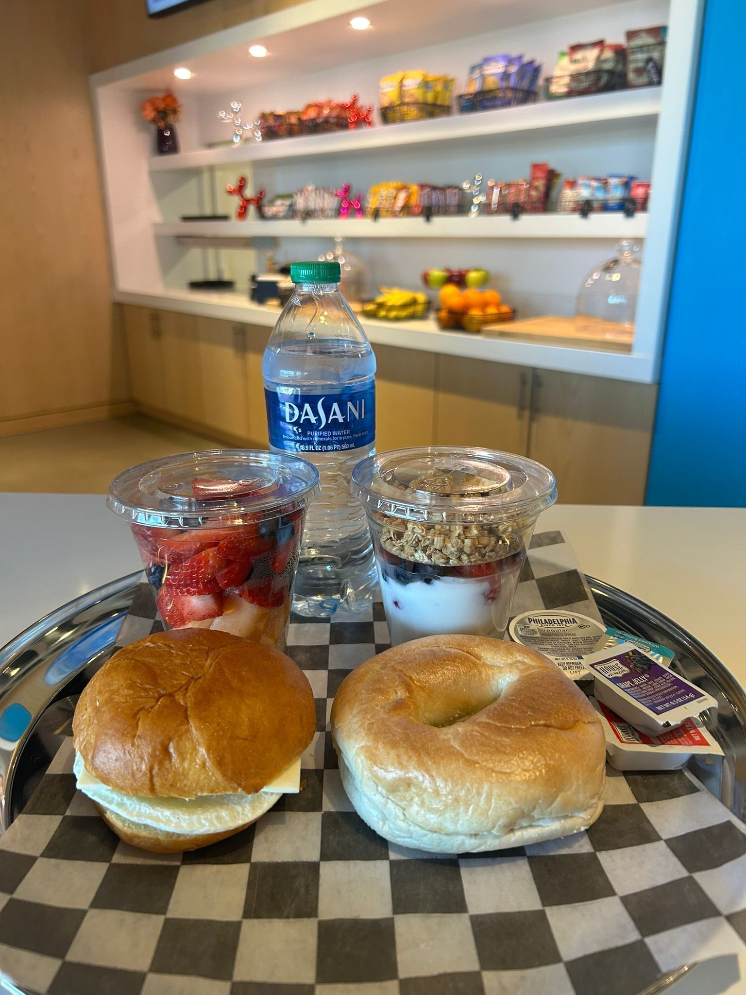 Ein Tablett mit einem Beutel, einem Sandwich, einer Flasche Dasani Wasser und zwei Portionen Joghurt-Parfaits.