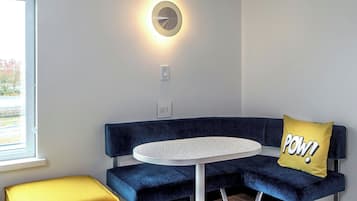A modern room with a round table, a blue sofa, and a yellow pillow with "POW!" text.