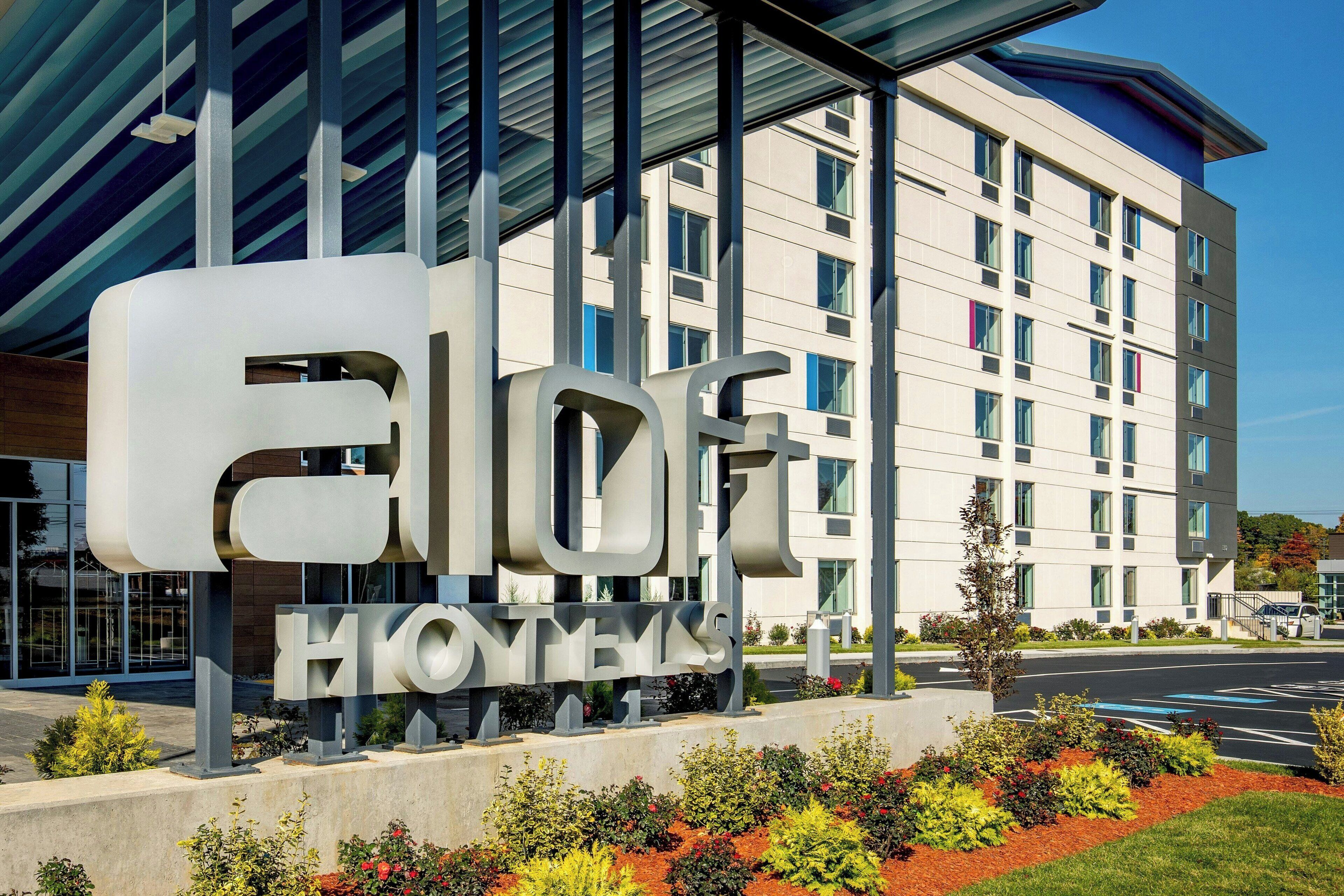 A hotel sign with the name "ELOFT HONEYVAH" and a modern building in the background.