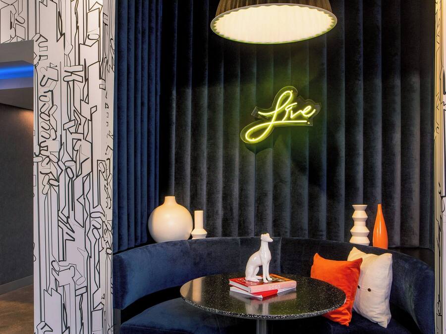 A modern lounge area with a dark blue sofa, a round table with a book and a decorative item, and a neon sign on the wall.