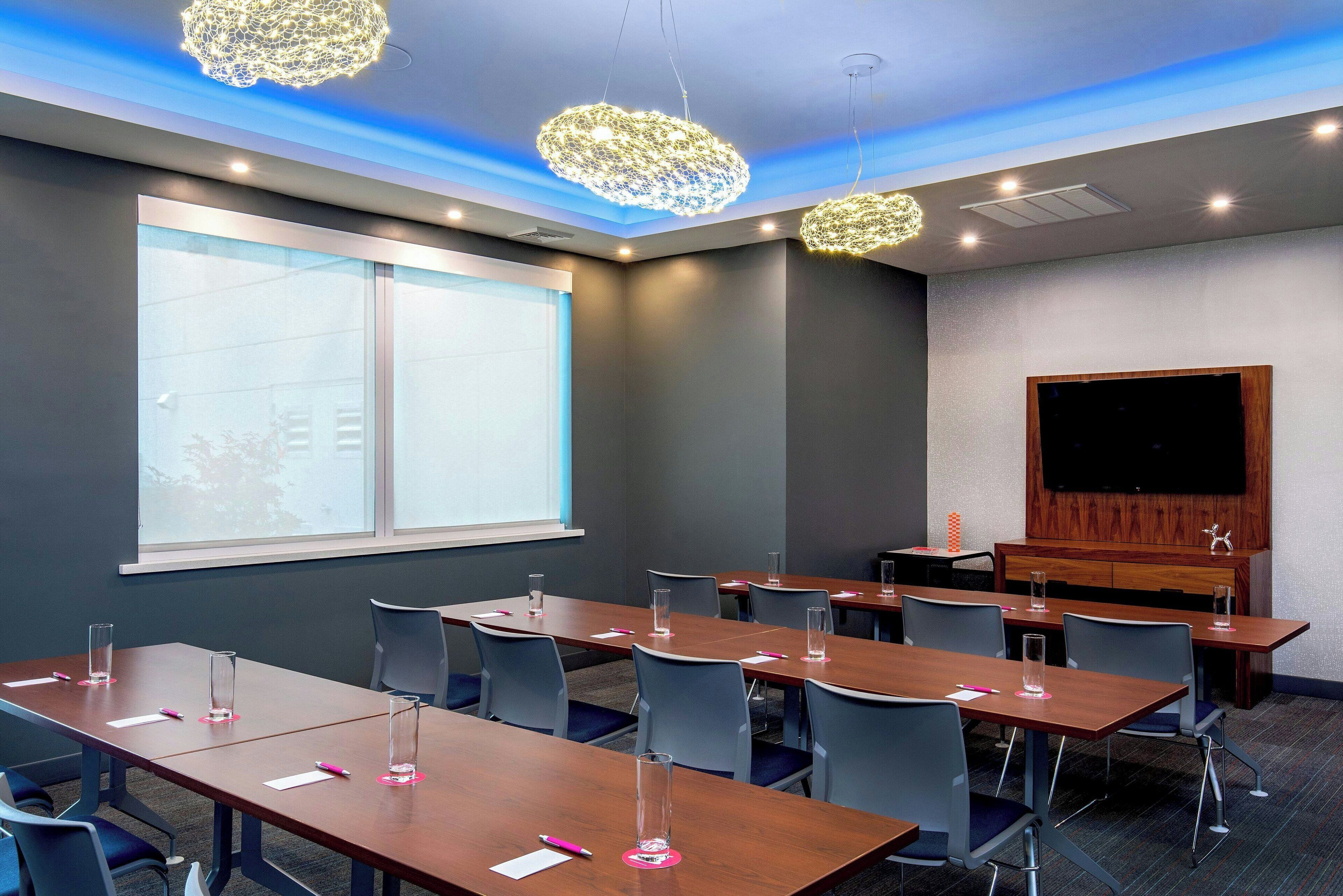 A conference room with long tables, chairs, and a large screen.