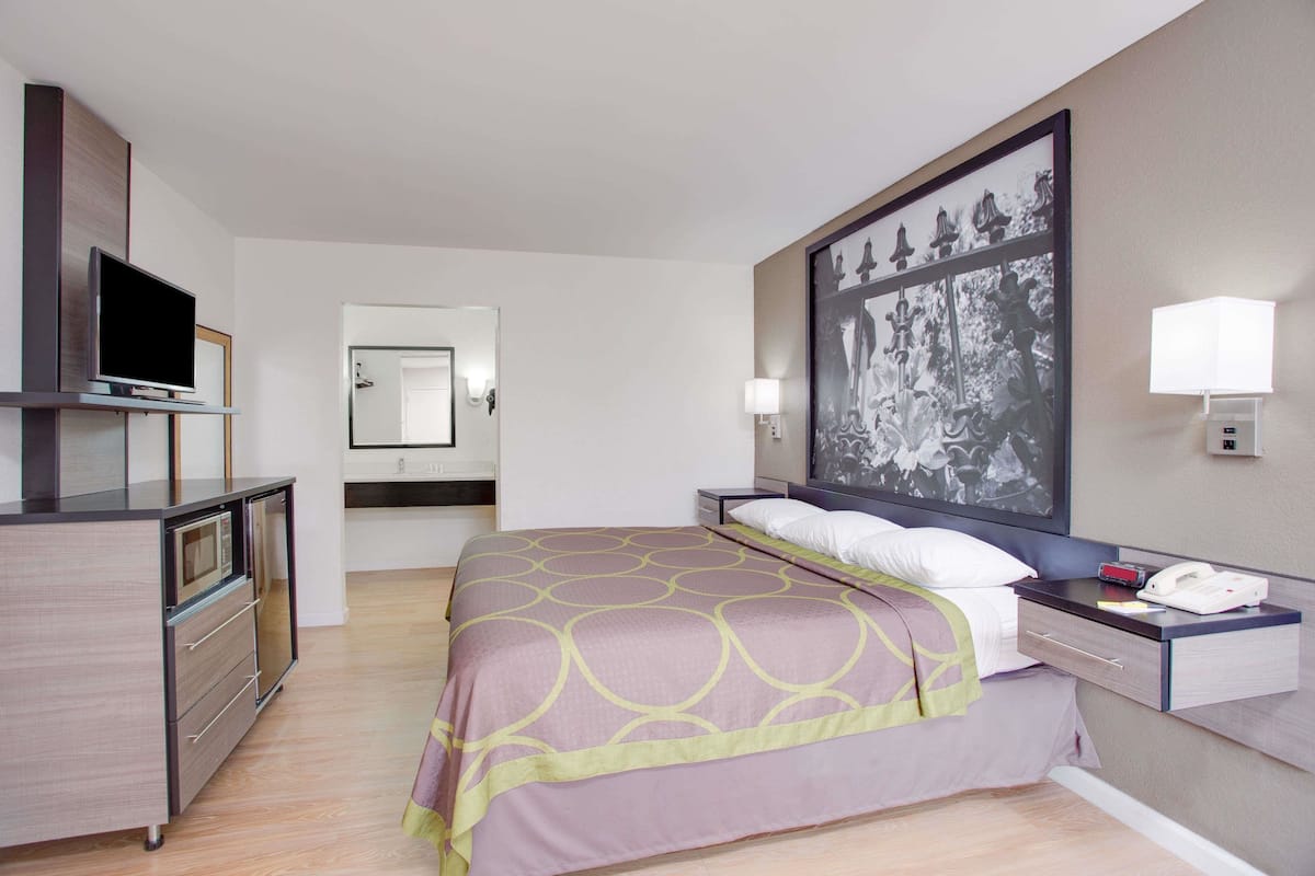 Ein Hotelzimmer mit einem Bett, einem Fernseher, einem Schreibtisch, einer Lampe und einem großen Bild in einem Rahmen an der Wand.