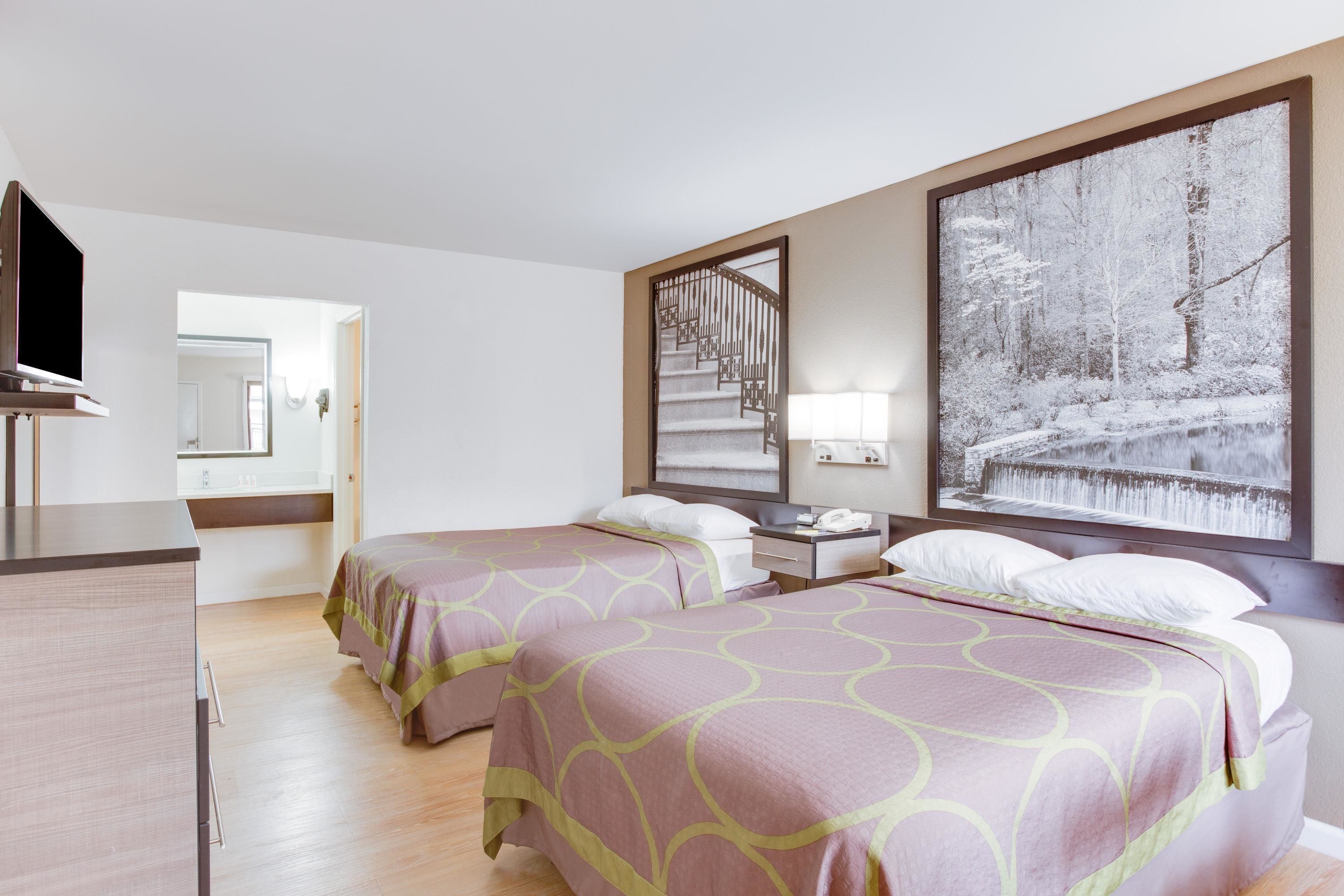 Habitación de hotel con dos camas, televisión, escritorio, espejo y un amplio ventanal con vistas a un paisaje nevado.