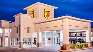 A Super 8 hotel with a modern design, featuring a central entrance with glass doors, a covered parking area, and a clear sky in the background. - Super 8 by Wyndham Dalton (Dalton)
