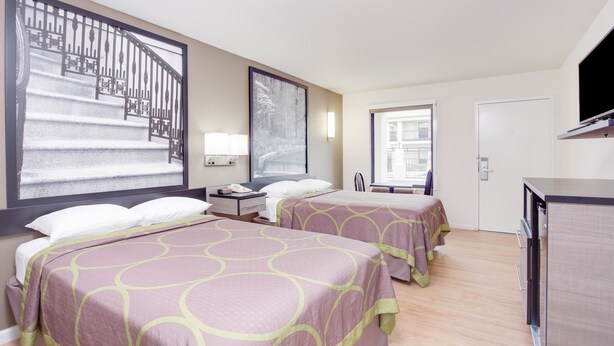 A hotel room with two beds, a desk, a TV, and a large window with a view of a building. - Super 8 by Wyndham Dalton (Dalton)
