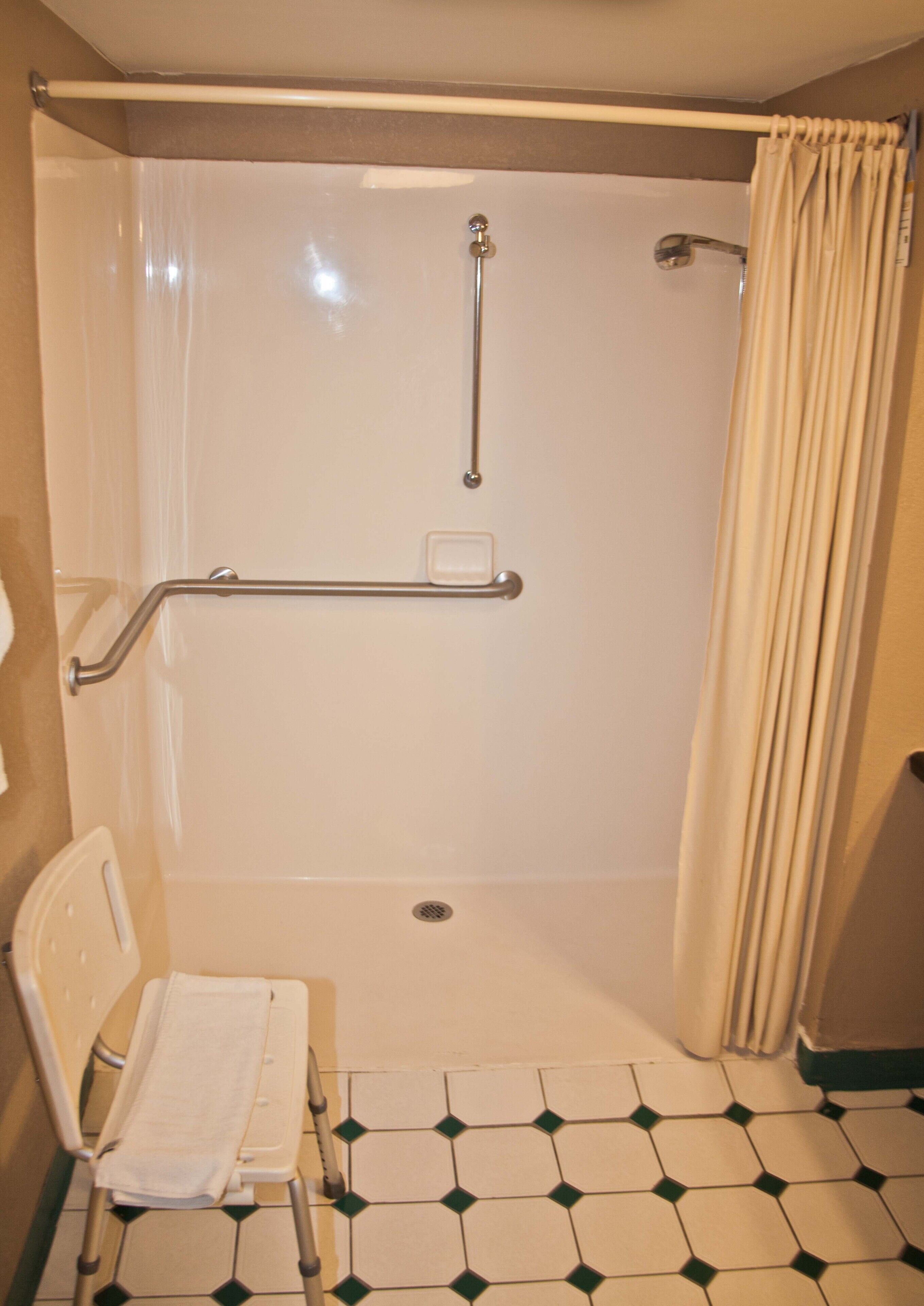 A bathroom with a shower, grab bars, a wheelchair-accessible bench, and a tiled floor.