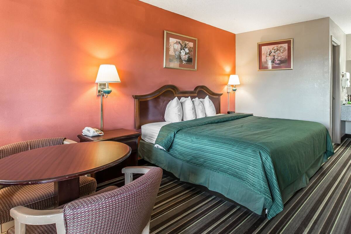 A hotel room with a bed, a desk, a chair, and two lamps.