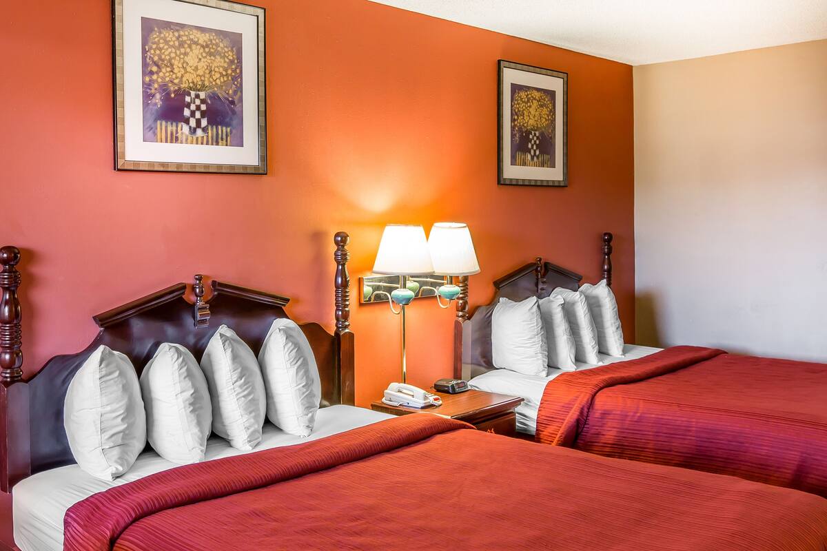 A hotel room with two beds, a nightstand with a lamp, and two framed pictures on the wall.