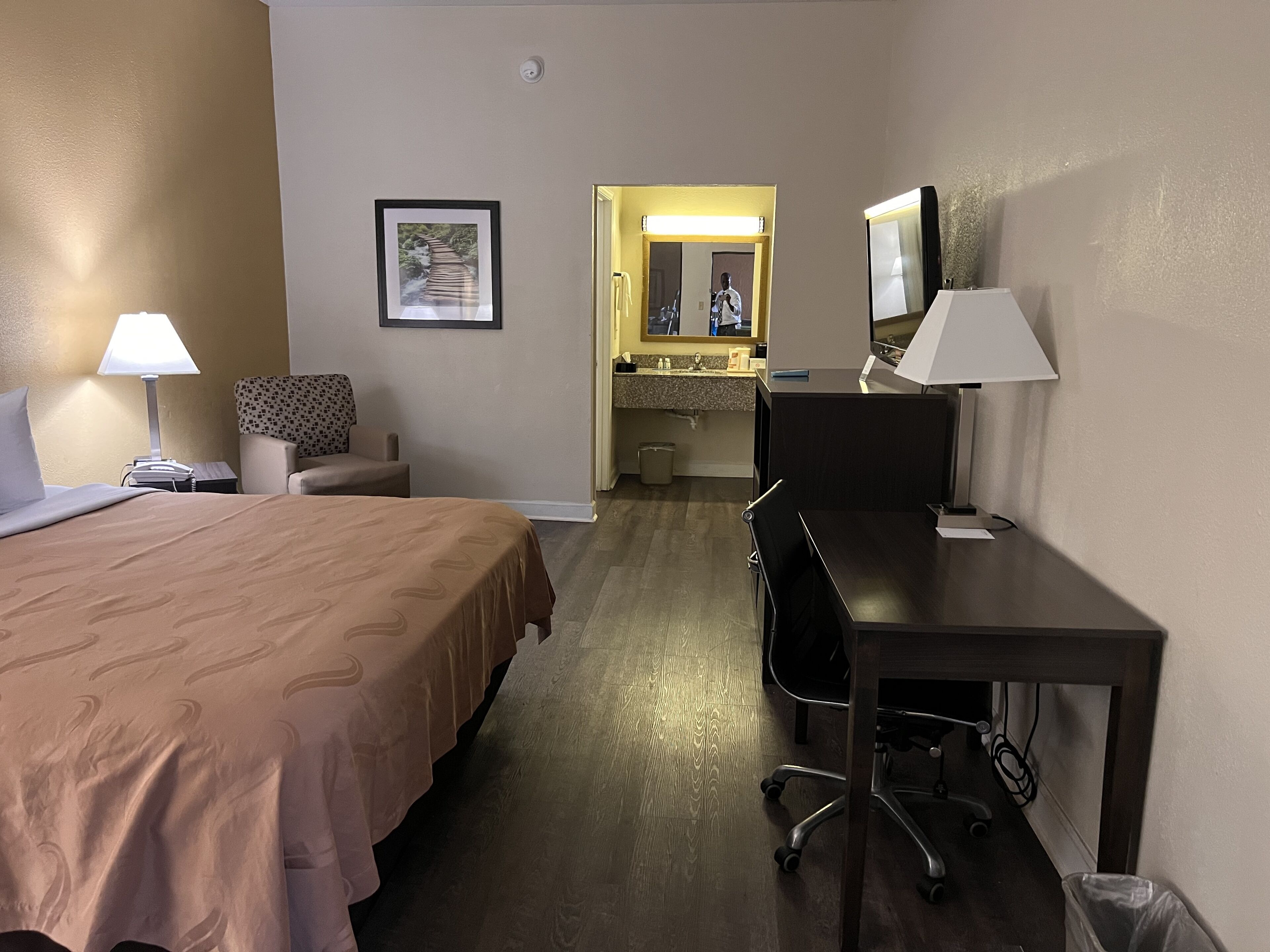 Ein Hotelzimmer mit Bett, Schreibtisch, Stuhl und einem durchgegangenen Tür sichtbaren Badezimmer.