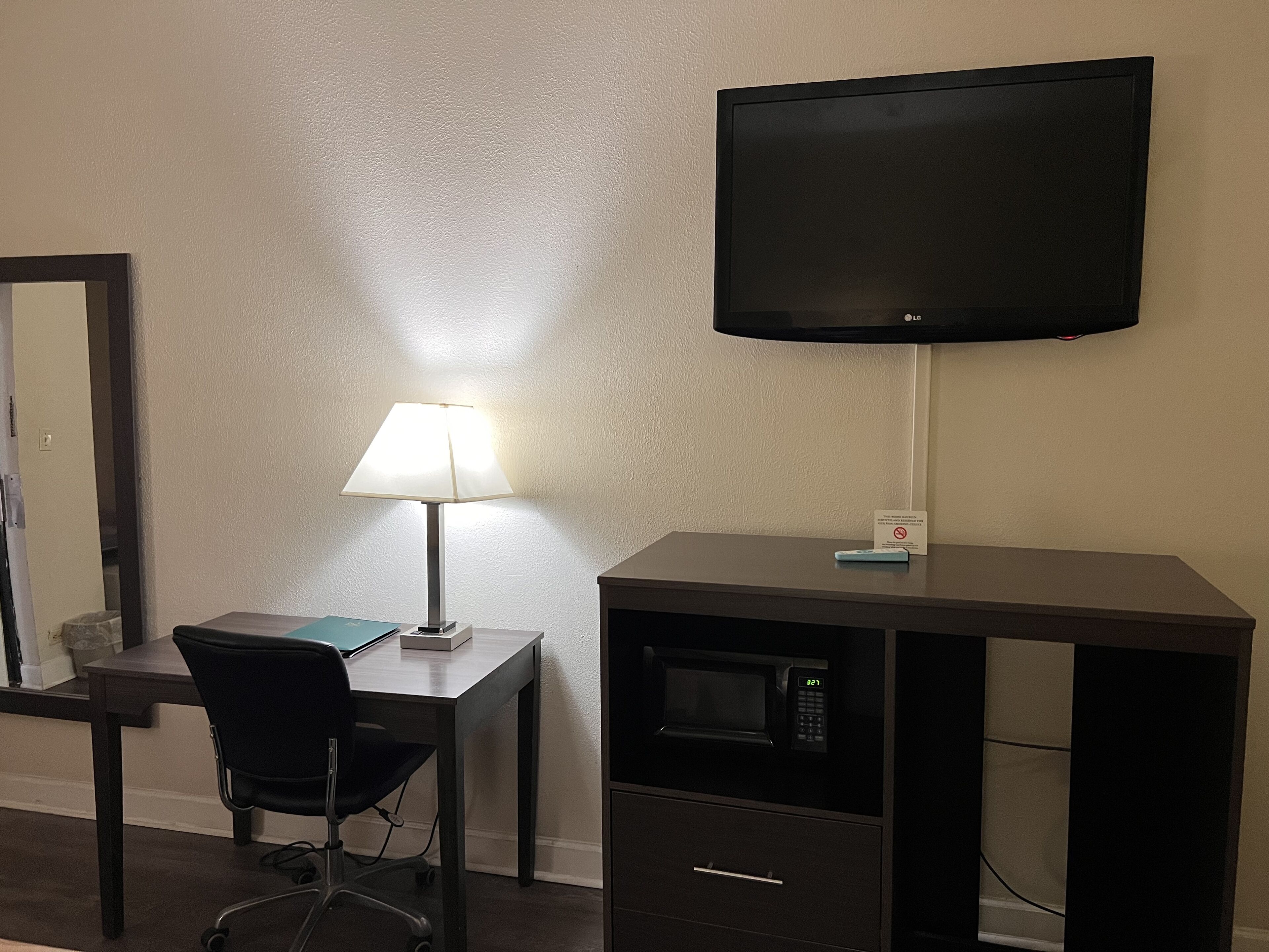 Habitación de hotel con escritorio, silla, lámpara, televisión y microondas.