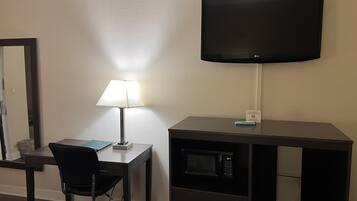 Habitación de hotel con escritorio, silla, lámpara, televisión y microondas.