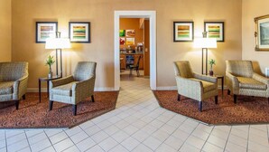 A hotel lobby with two armchairs, a coffee table, and a dining area in the background.
