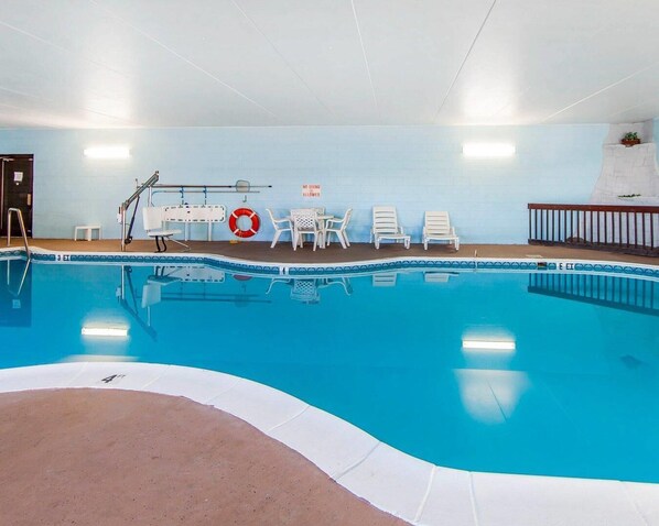 Una piscina interior con un flotador salvavidas, sillones de descanso y un cartel que indica prohibido bucear.