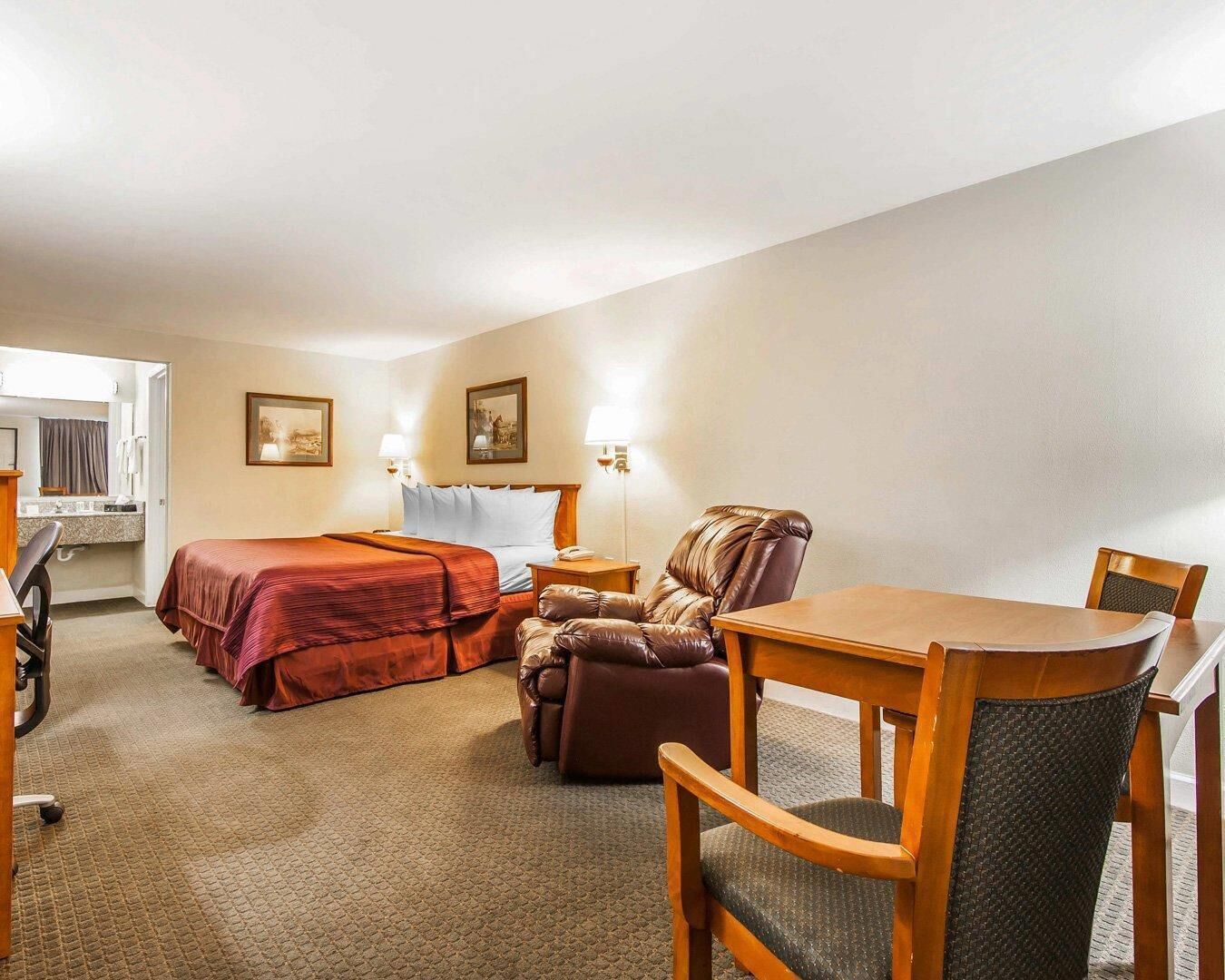A hotel room with two beds, a desk, a chair, and a small table.