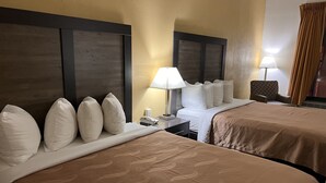 A hotel room with two beds, a nightstand, a lamp, and a chair.