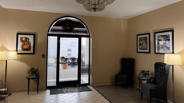 A hotel lobby with a chandelier, framed artwork, a reception desk, and a chair.