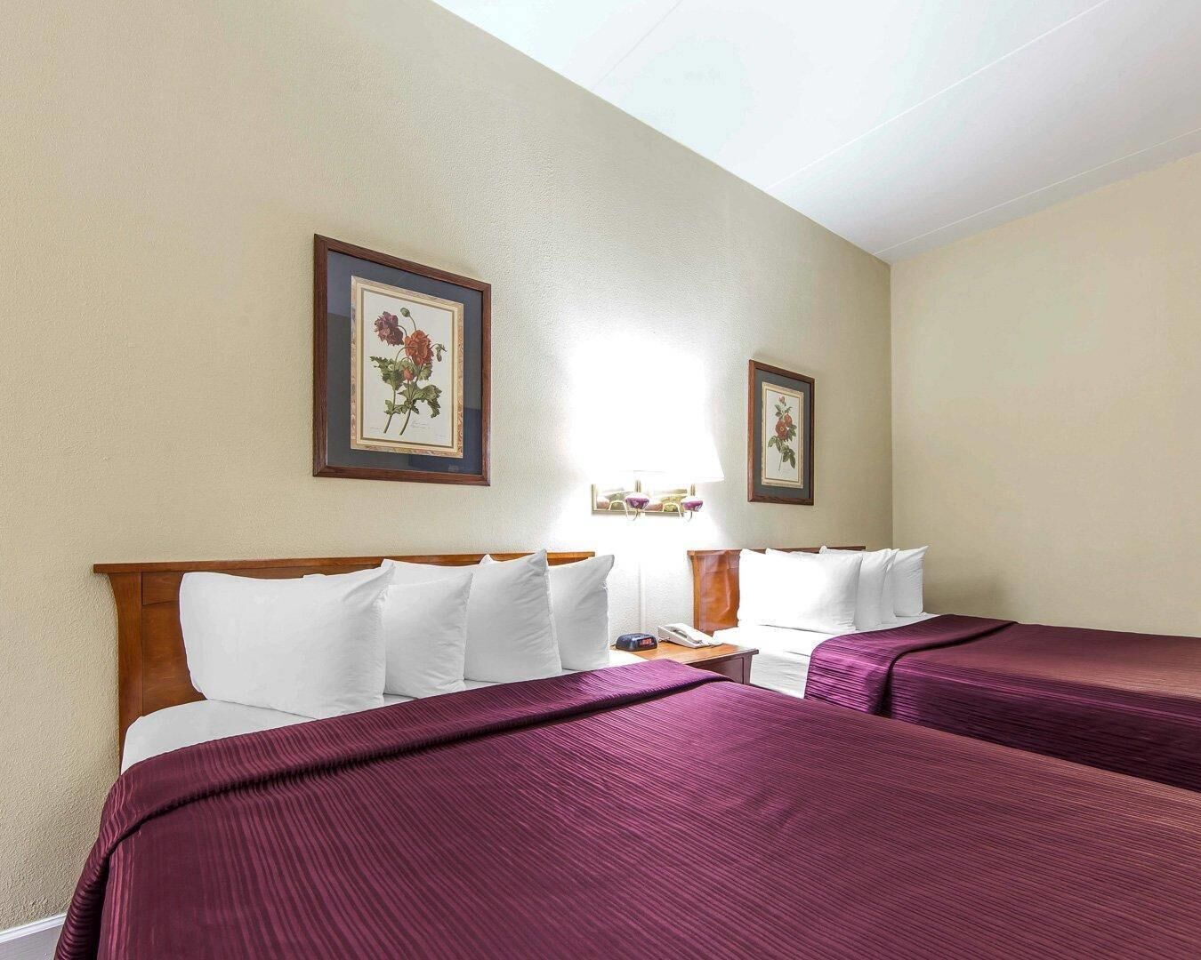 A hotel room with two beds, a wooden headboard, and two framed floral pictures on the wall.