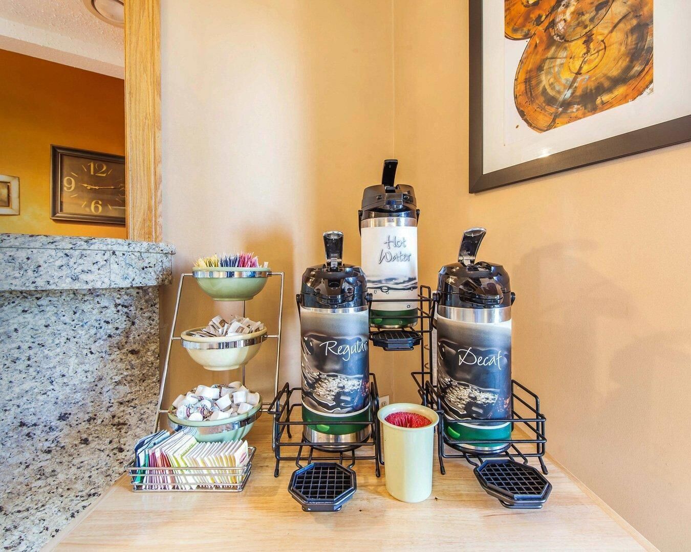A coffee station with a coffee machine, a hot water dispenser, and a decaf coffee dispenser. There are also bowls of sugar and a tray of napkins.