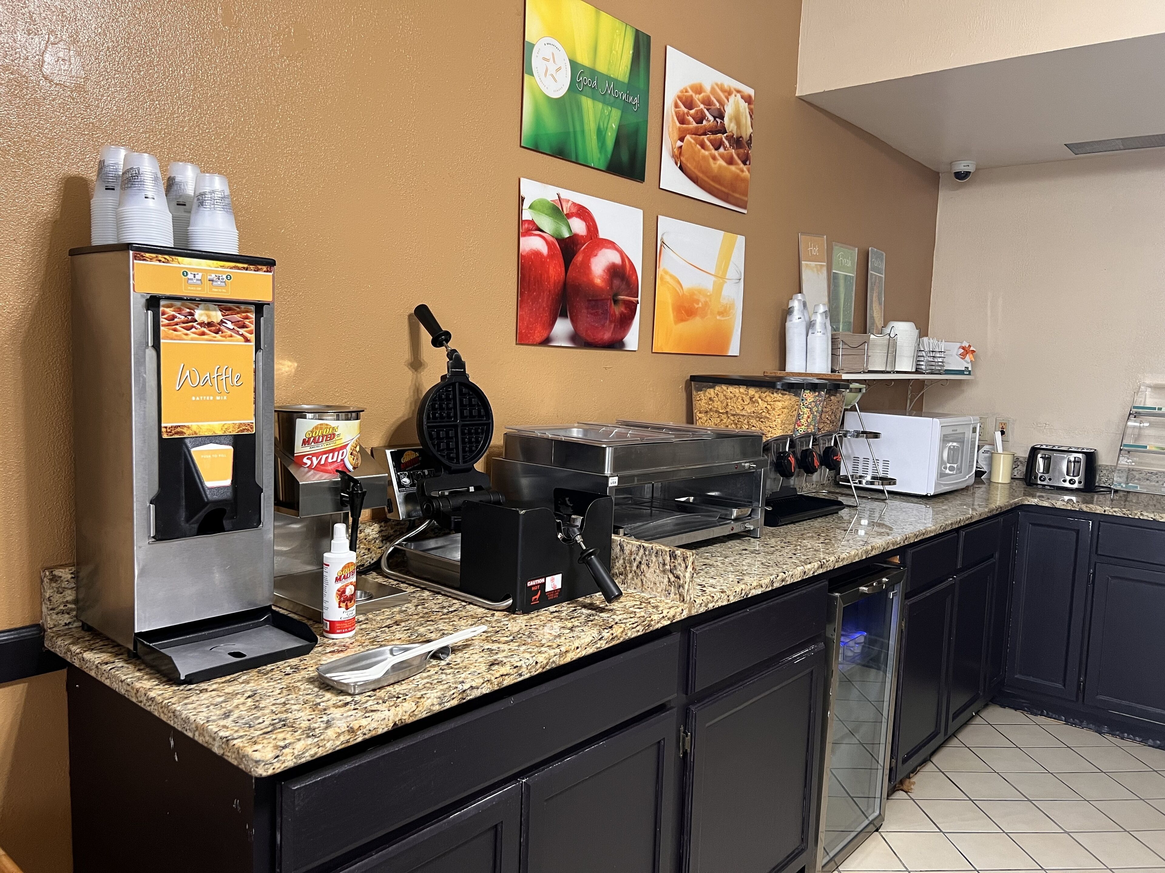 A breakfast bar with waffle and syrup dispensers, a waffle maker, a toaster, and a coffee machine.