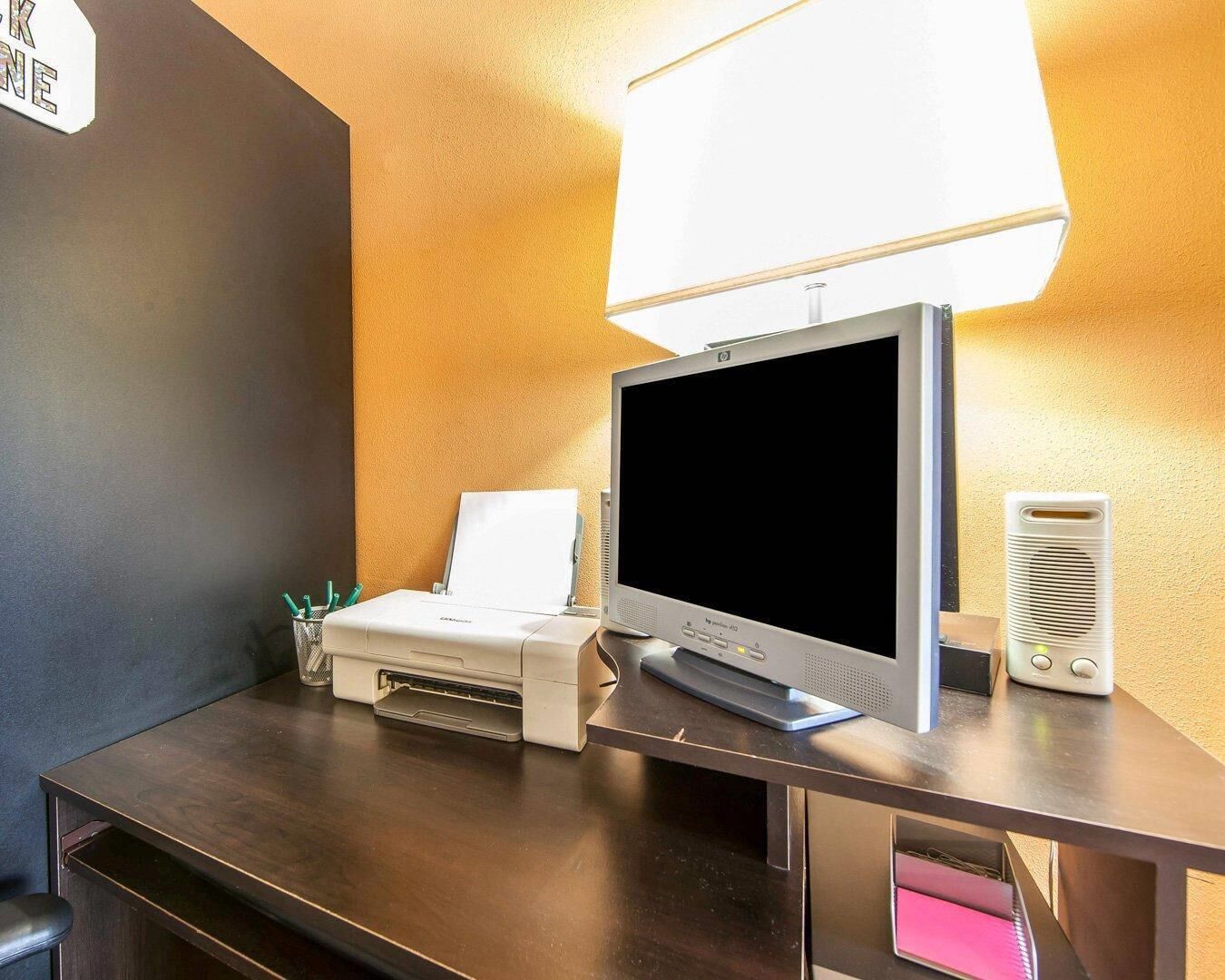 Et hotelværelse med skrivebord, printer, fladskærms-TV, lampe og højttaler.