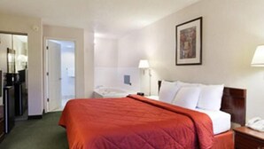 Una habitación de hotel con una cama, un escritorio, una silla, una lámpara y una puerta.